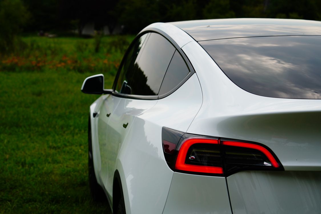 White Tesla Model Y rear three-quarter view in a green outdoor setting
